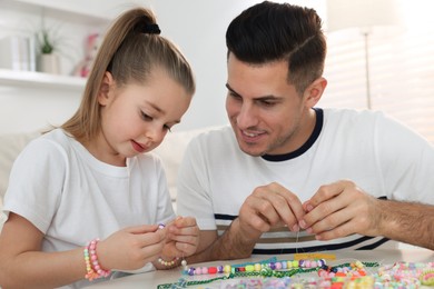 Photo of Happy father with his cute daughter making beaded jewelry at table in room