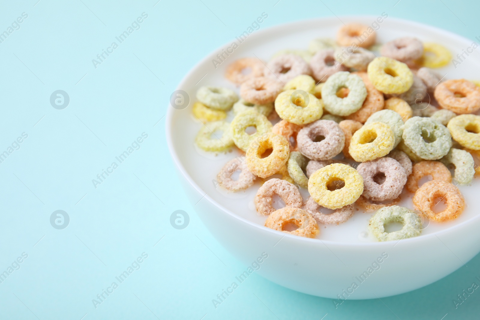 Photo of Tasty colorful cereal rings and milk in bowl on turquoise background, closeup. Space for text