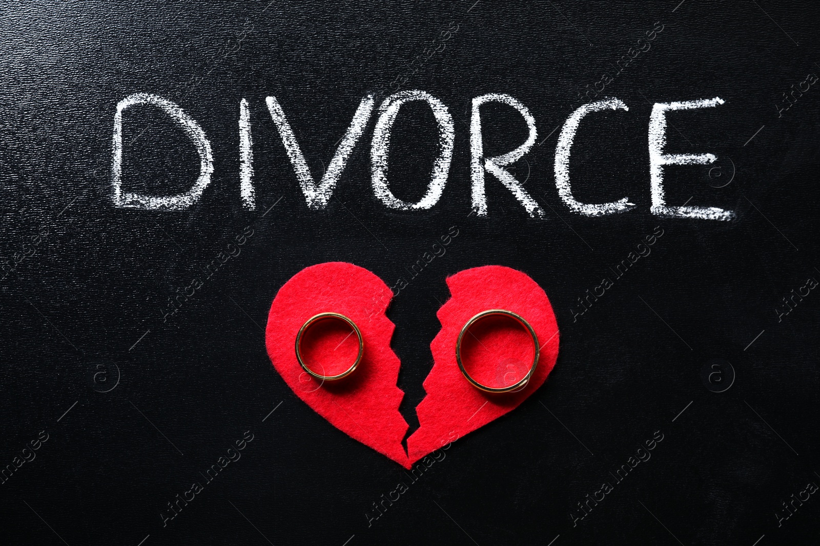 Photo of Word Divorce, broken red paper heart and wedding rings on blackboard, top view