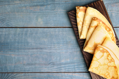 Fresh thin pancakes on blue wooden table, top view. Space for text