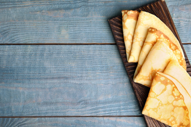 Photo of Fresh thin pancakes on blue wooden table, top view. Space for text