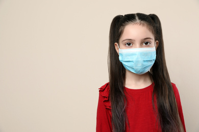 Little girl in medical mask on beige background, space for text. Virus protection