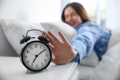 Photo of Young woman turning off alarm clock at home in morning, focus on hand