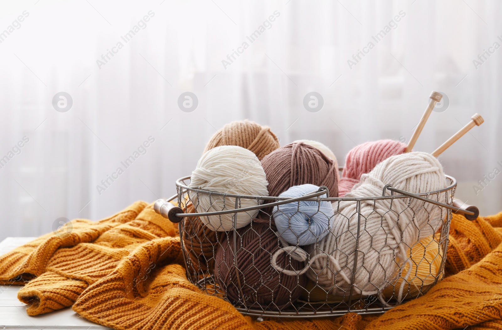 Photo of Soft woolen yarns with knitting needles and sweater on table indoors, space for text