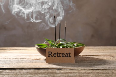 Photo of Card with word Retreat, green leaves and incense sticks on wooden table