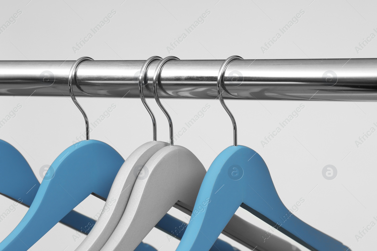 Photo of Empty clothes hangers on metal rail against light background, closeup