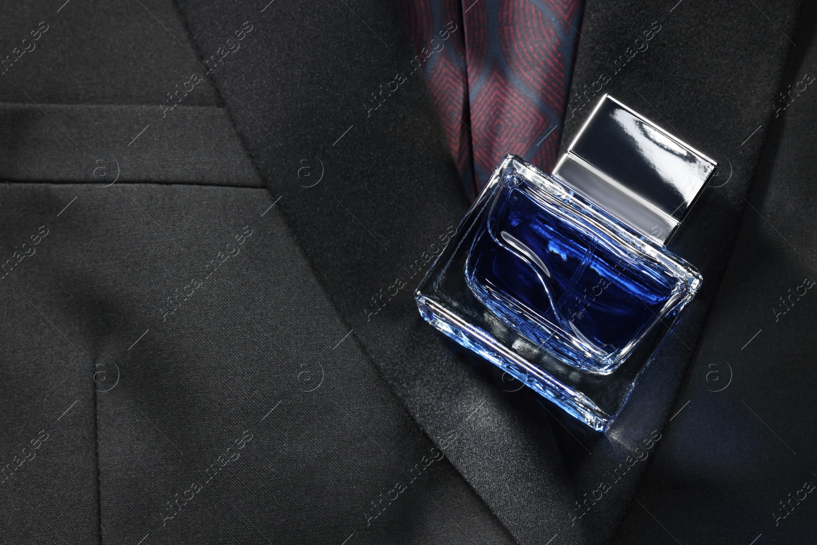 Photo of Luxury men's perfume in bottle on black jacket, above view. Space for text