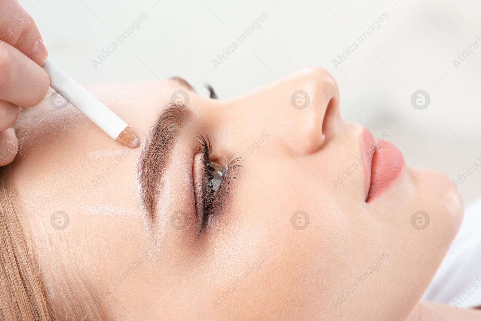 Photo of Cosmetologist preparing young woman for  eyebrow permanent makeup procedure, closeup