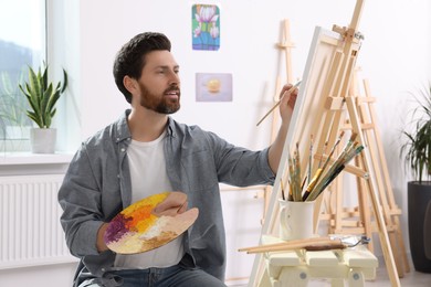 Photo of Man painting in studio. Using easel to hold canvas