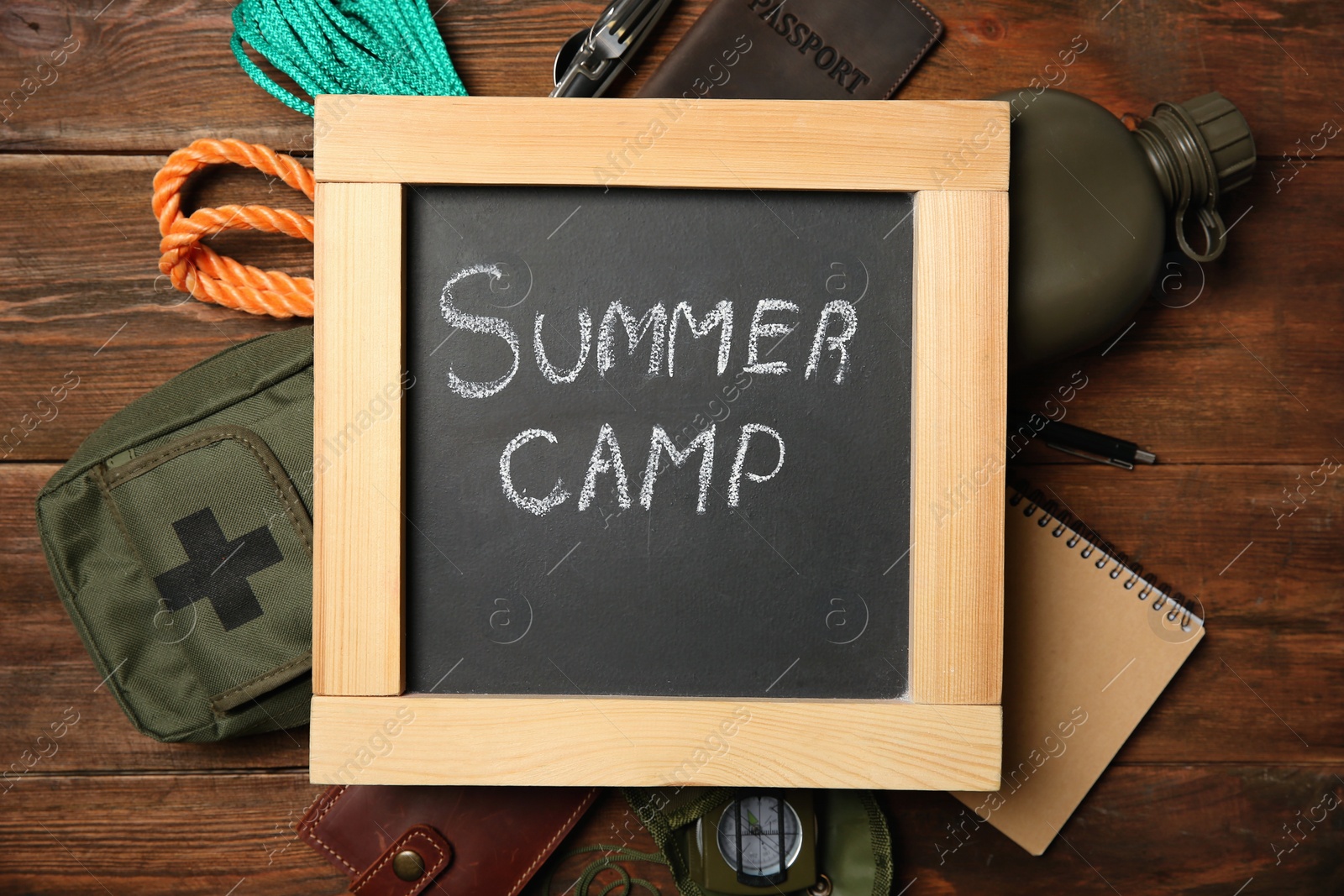 Photo of Chalkboard with text SUMMER CAMP and camping equipment on wooden background, flat lay