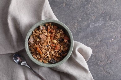 Tasty granola in bowl, spoon and napkin on gray textured table, flat lay. Space for text