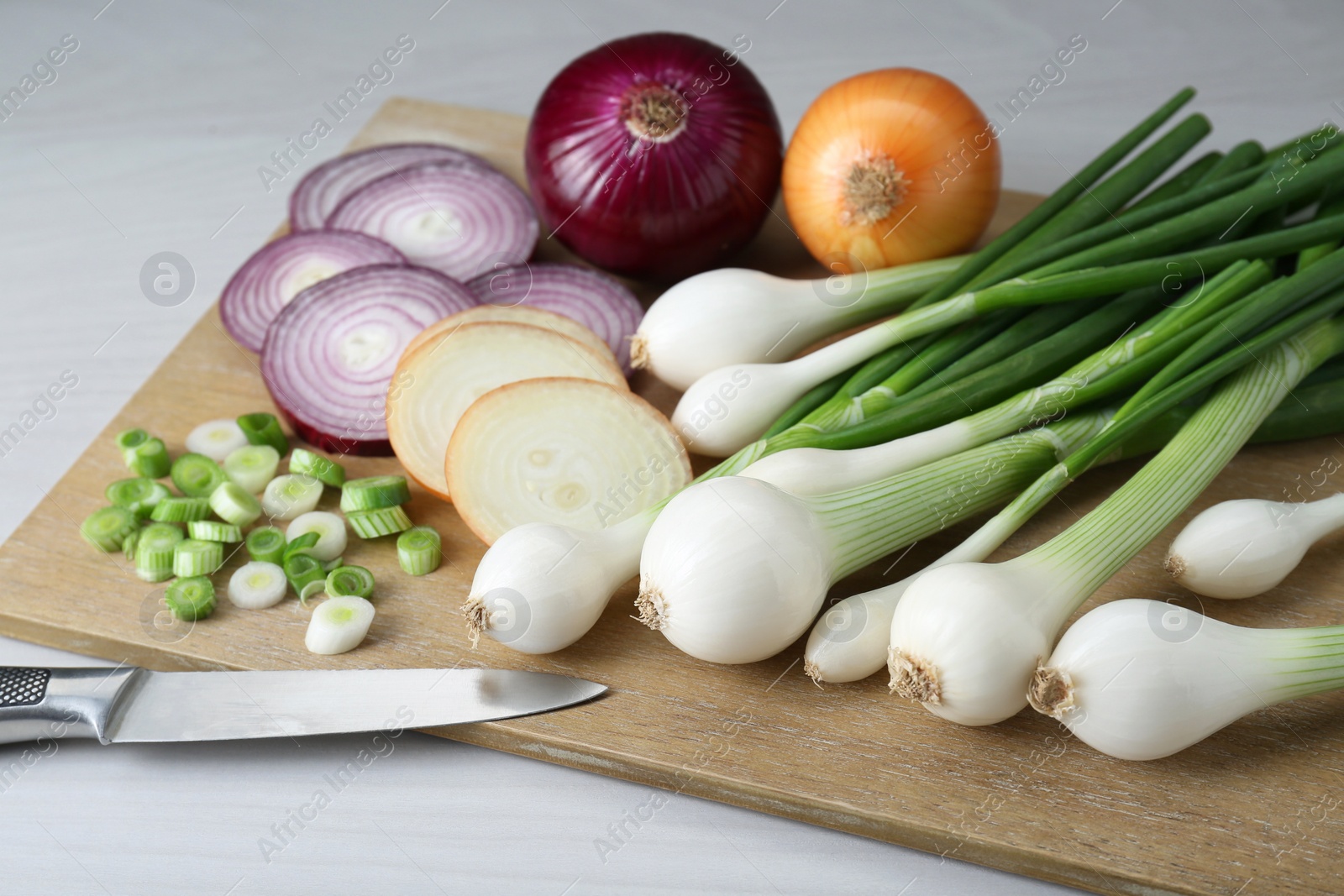 Photo of Board with different kinds of onions on white wooden table, closeup