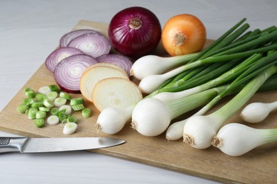 Board with different kinds of onions on white wooden table, closeup