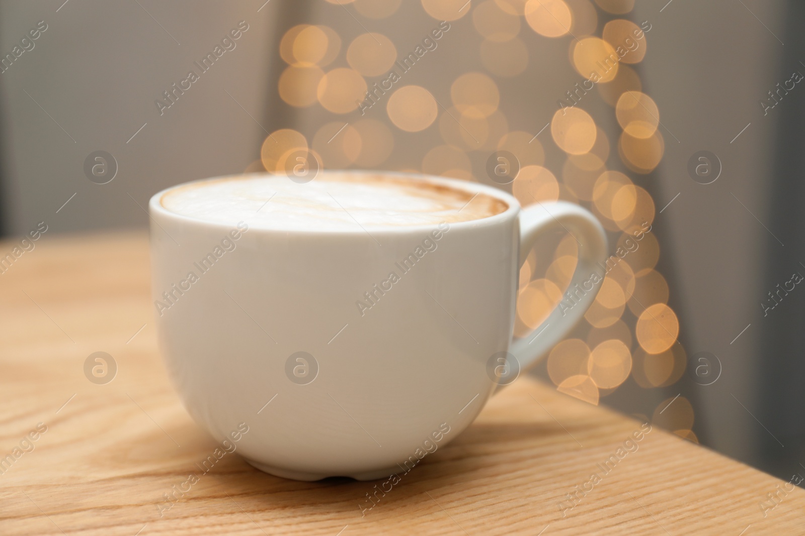 Photo of Cup of aromatic cacao on table against blurred lights