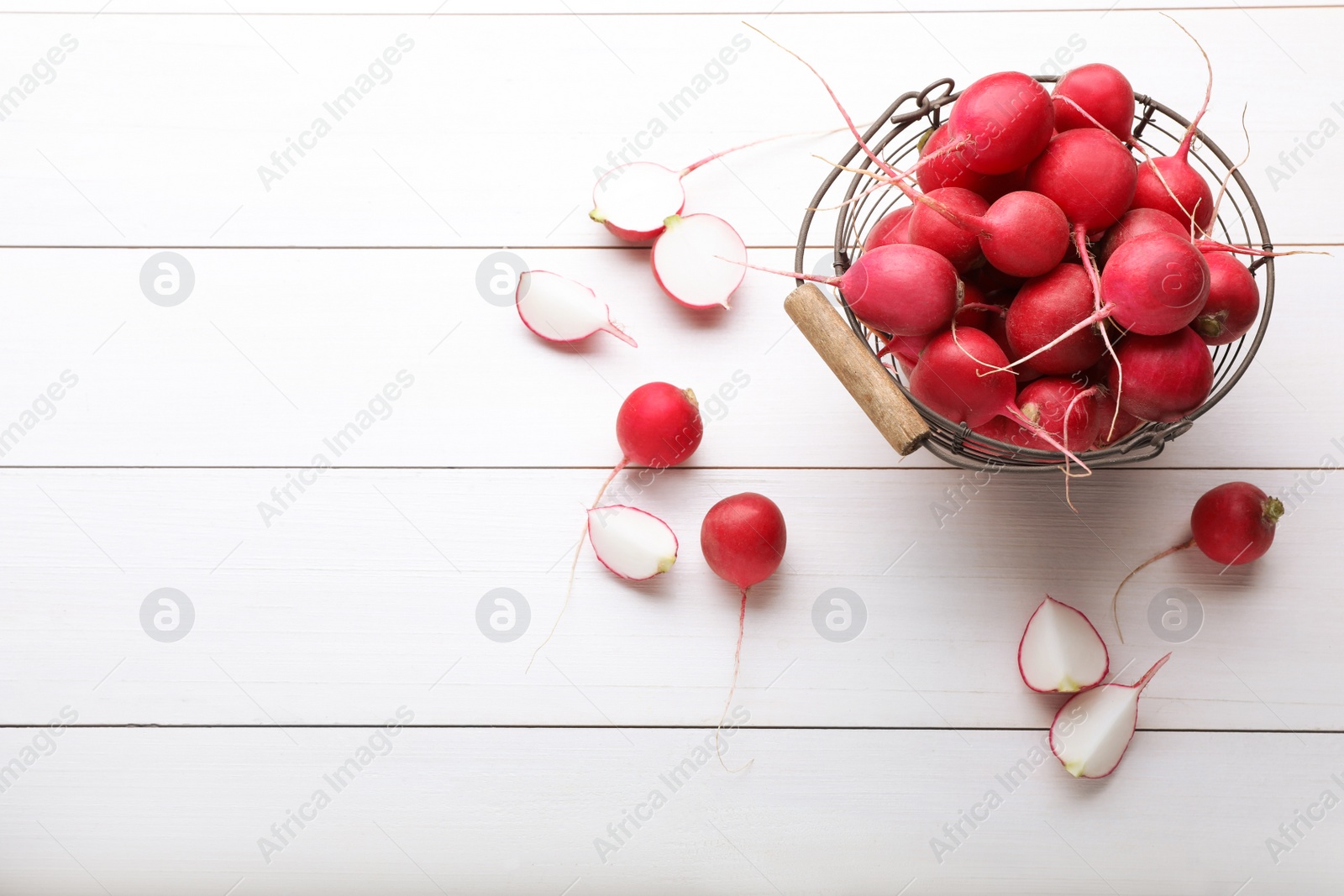 Photo of Metal basket with fresh ripe radishes on white wooden table, flat lay. Space for text