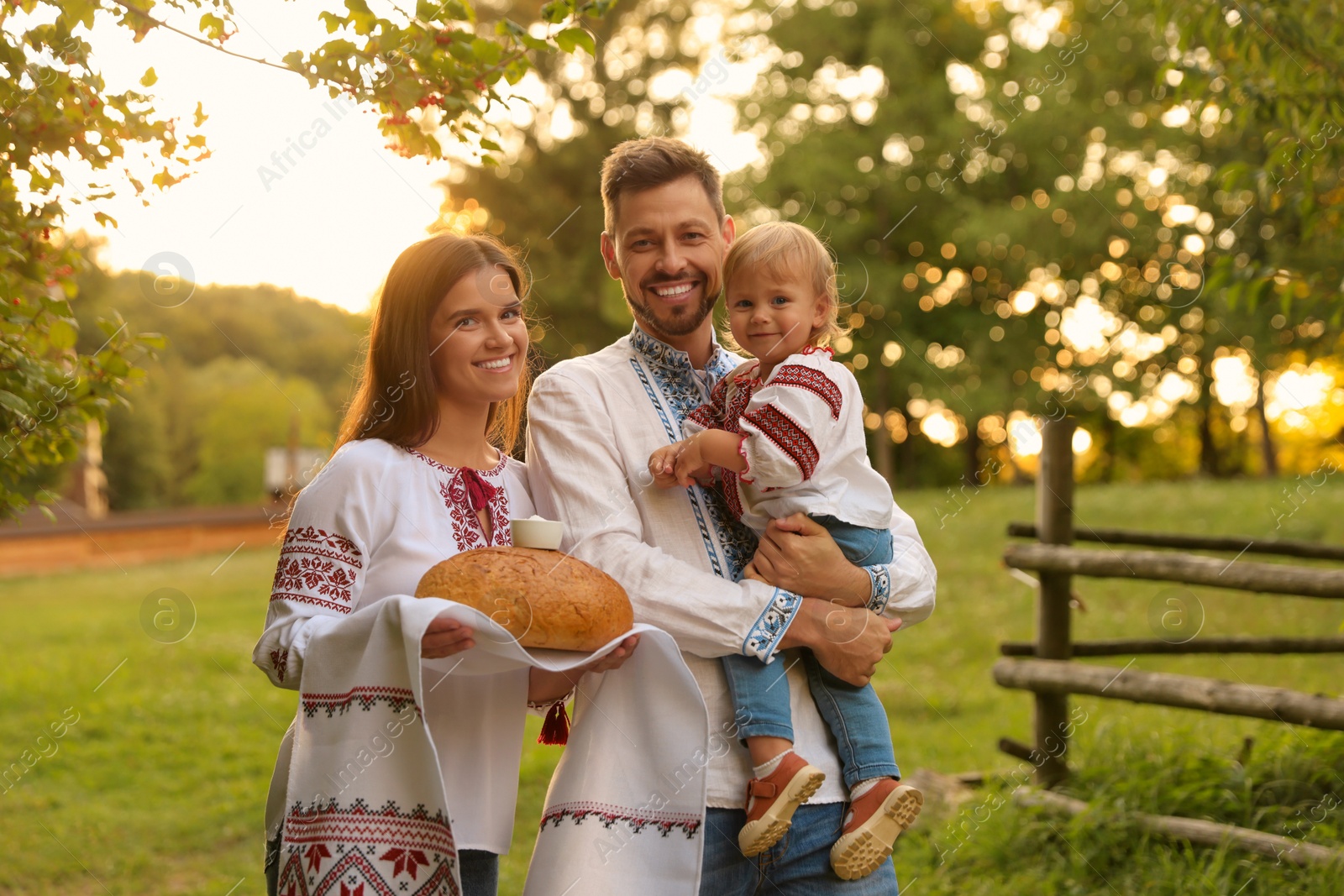 Photo of Happy cute family in embroidered Ukrainian shirts with korovai bread on sunny day