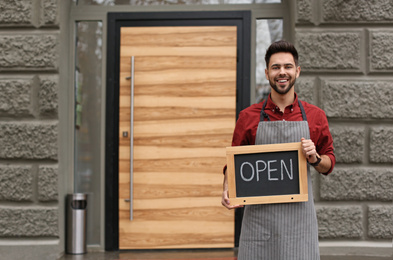 Photo of Young male business owner holding OPEN sign near his cafe. Space for text
