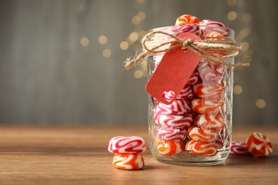 Photo of Color hard candies in glass jar on wooden table. Space for text