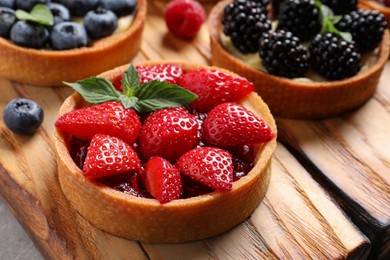 Tartlet with fresh strawberries on wooden board, closeup. Delicious dessert