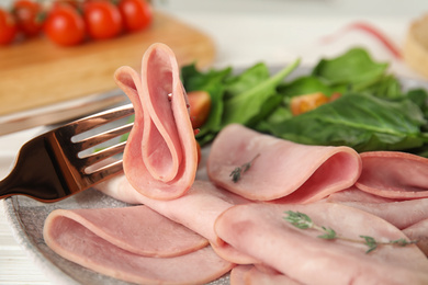 Photo of Fork with tasty ham on table, closeup