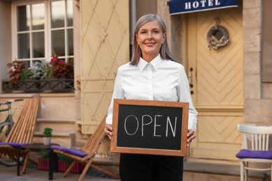 Photo of Happy business owner holding open sign near her hotel outdoors
