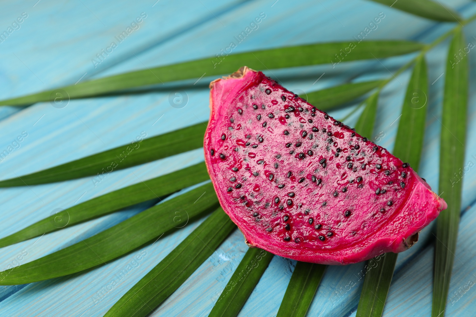 Photo of Delicious cut red pitahaya fruit and palm leaf on light blue wooden table, closeup