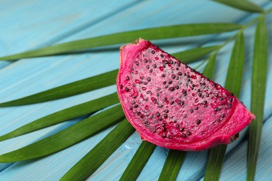 Photo of Delicious cut red pitahaya fruit and palm leaf on light blue wooden table, closeup