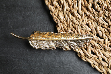 Beautiful gold hair clip and wicker mat on black table, top view