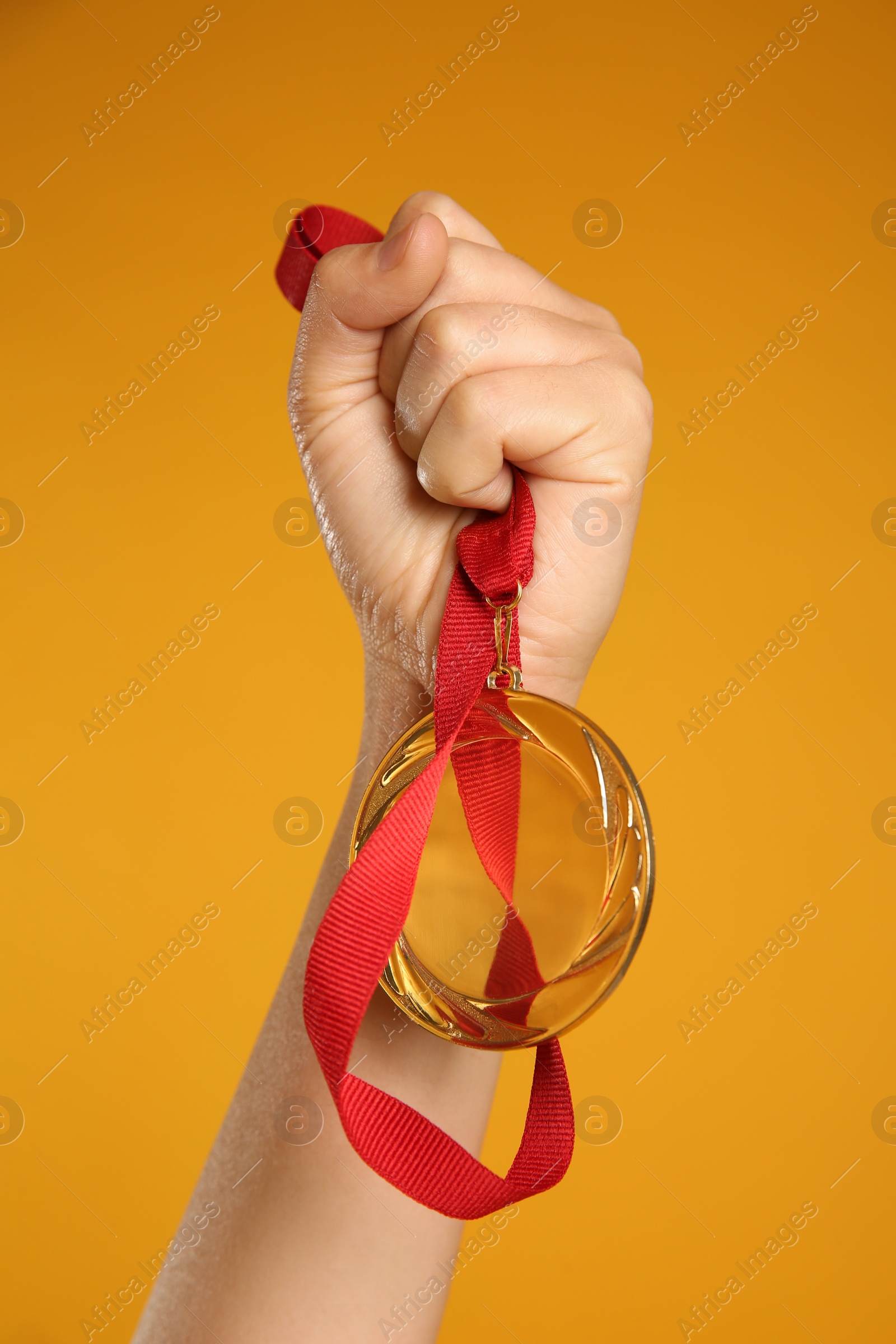 Photo of Woman holding gold medal on yellow background, closeup