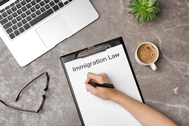 Woman filling form with words IMMIGRATION LAW at table, top view