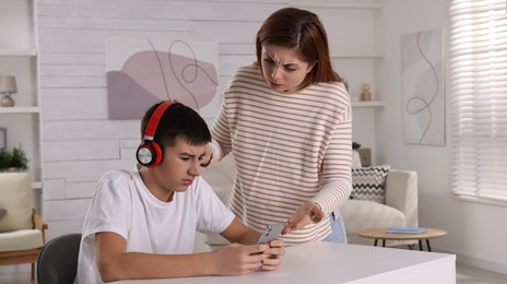 Photo of Mother scolding her son while he listening music in headphones at home. Teenager problems