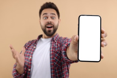 Surprised man showing smartphone in hand on beige background, selective focus. Mockup for design