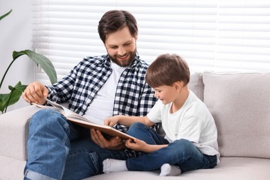 Happy dad and son reading book together on sofa at home