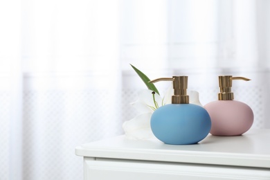 Photo of Stylish soap dispensers and lily on table against blurred background. Space for text