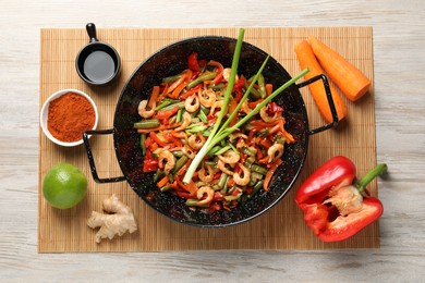 Shrimp stir fry with vegetables in wok and ingredients on wooden table, flat lay