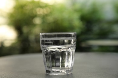 Photo of Glass of fresh water on grey table outdoors, closeup
