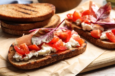 Serving board with tasty bruschettas on wooden table, closeup