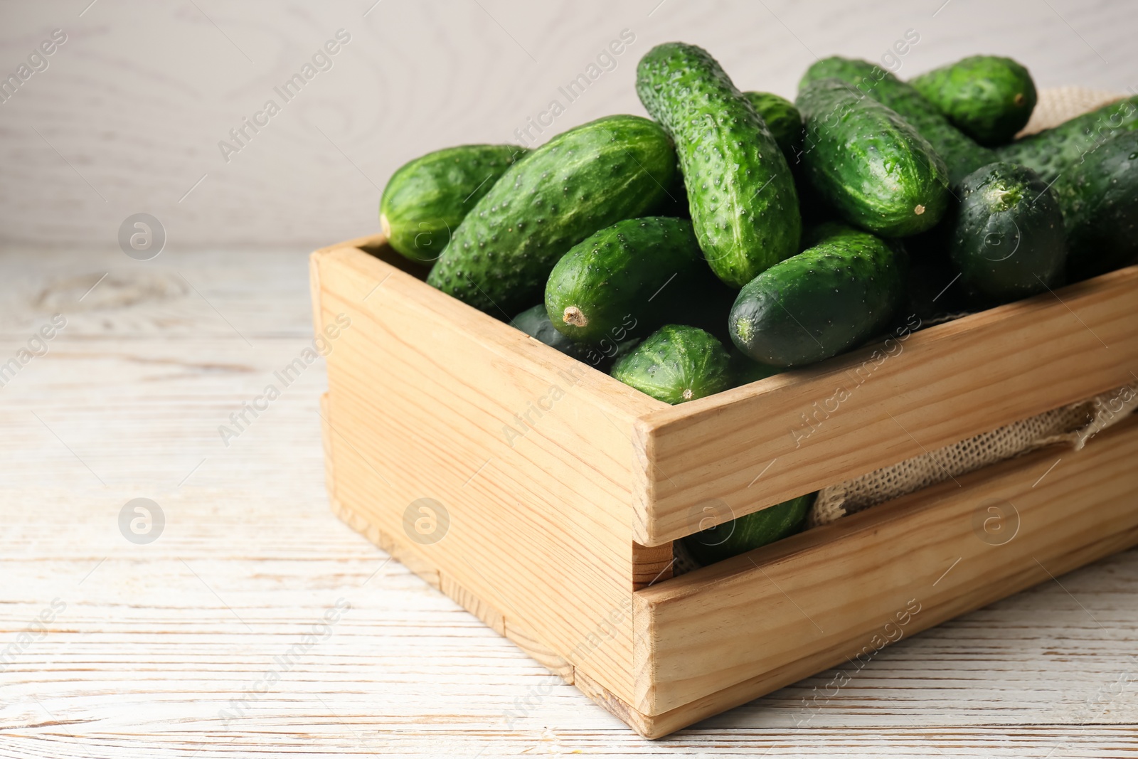 Photo of Crate full of fresh ripe cucumbers on white wooden table