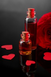 Photo of Bottles of love potion, paper hearts and red rose on mirror surface, closeup