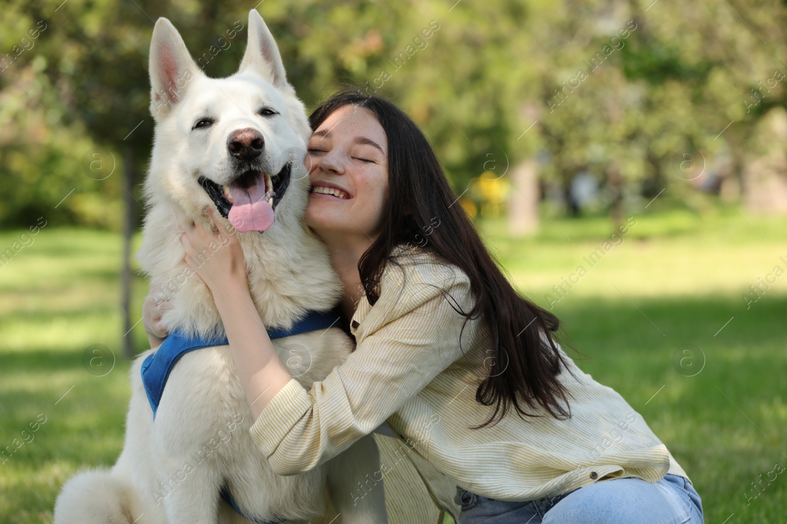 Photo of Teenage girl hugging her white Swiss Shepherd dog in park