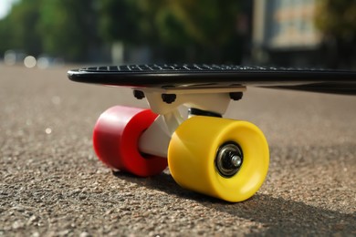 Black skateboard with colorful wheels on asphalt outdoors, closeup