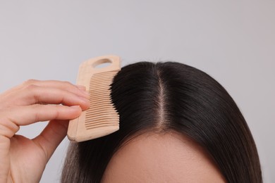 Photo of Woman with comb examining her hair and scalp on grey background, closeup