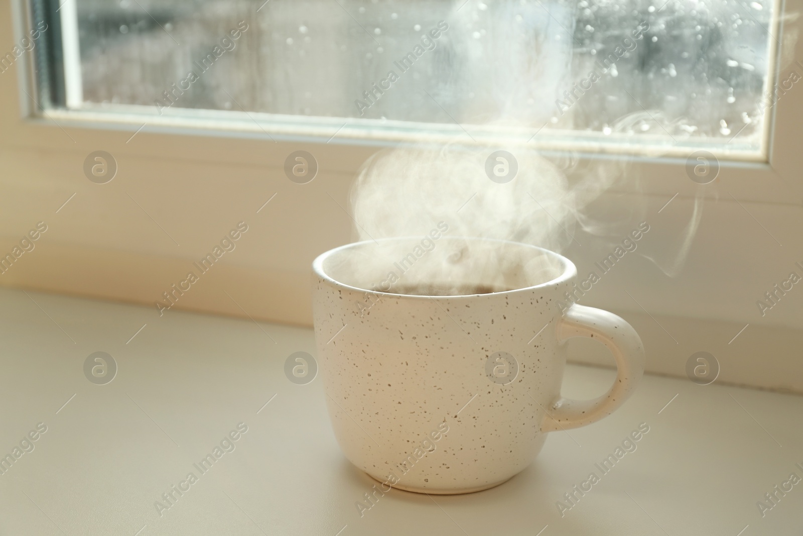 Photo of Cup of hot drink near window on rainy day