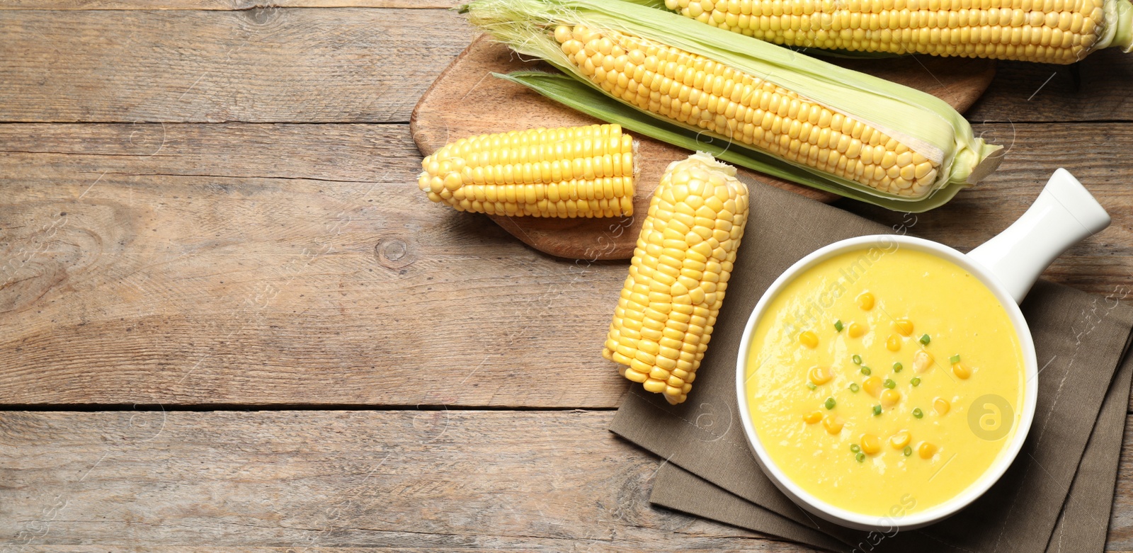 Photo of Delicious creamy corn soup and cobs on wooden table, flat lay. Space for text