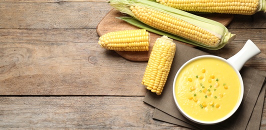 Delicious creamy corn soup and cobs on wooden table, flat lay. Space for text