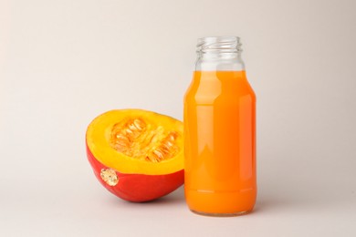 Photo of Tasty pumpkin juice in glass bottle and cut pumpkin on light background