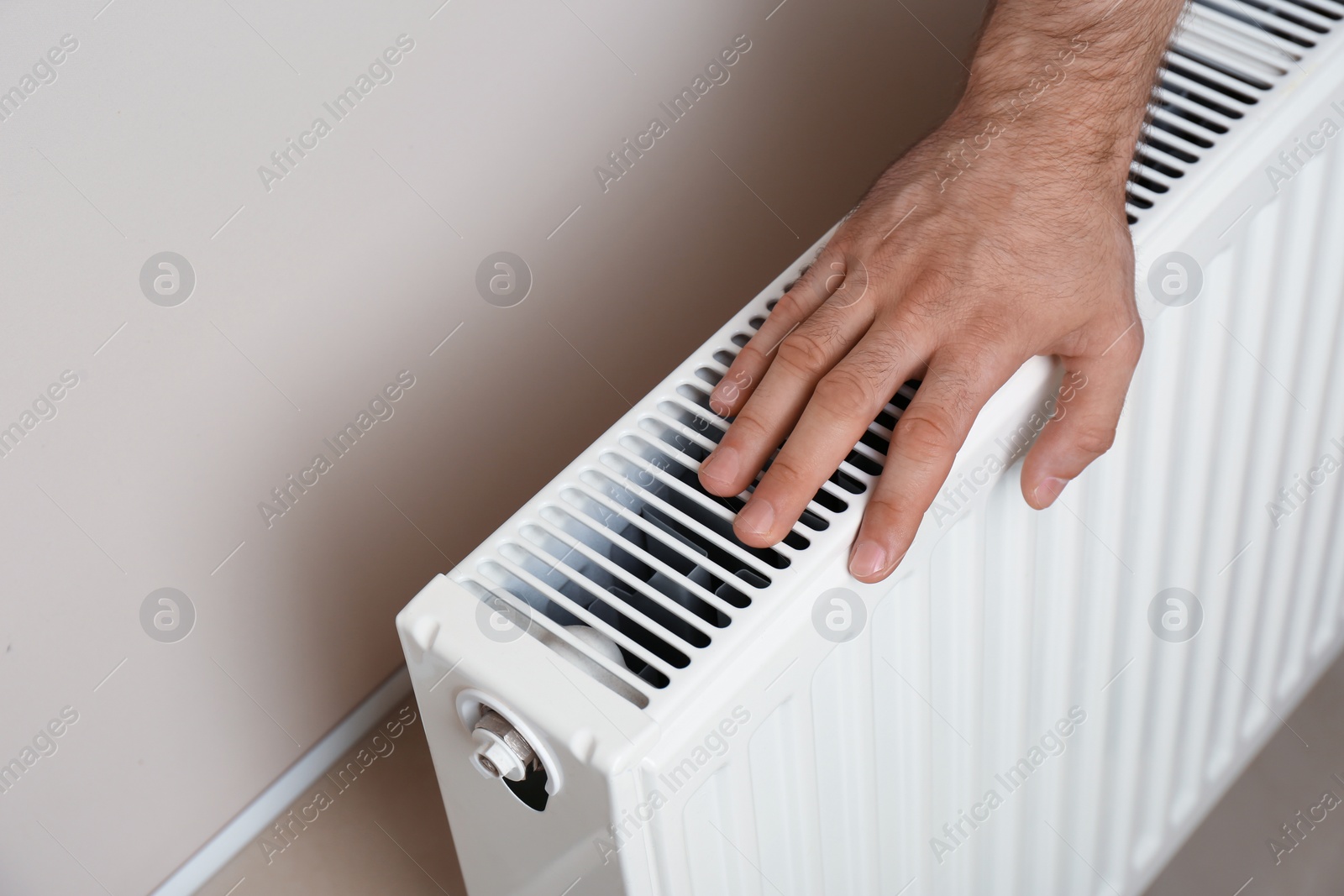 Photo of Man warming hand on heating radiator near color wall