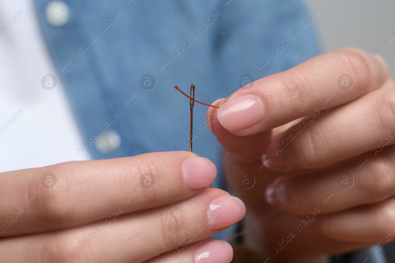 Photo of Woman inserting thread through eye of needle, closeup