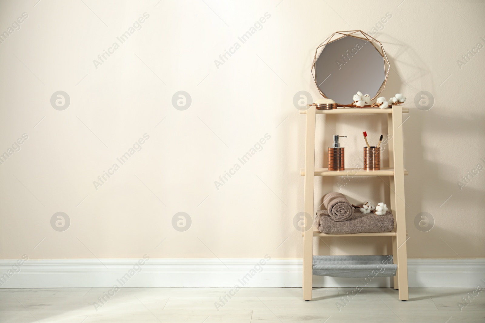 Photo of Wooden shelving unit with toiletries near beige wall indoors, space for text. Bathroom interior element