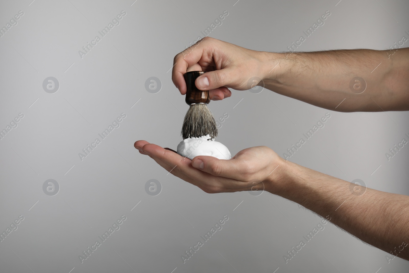 Photo of Man applying shaving foam onto brush on light grey background, closeup